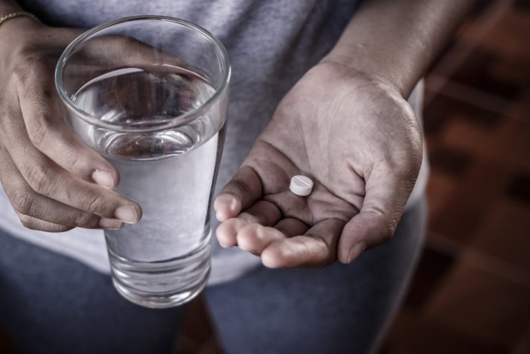 Close up of girl holding paracetamol and glass of water.