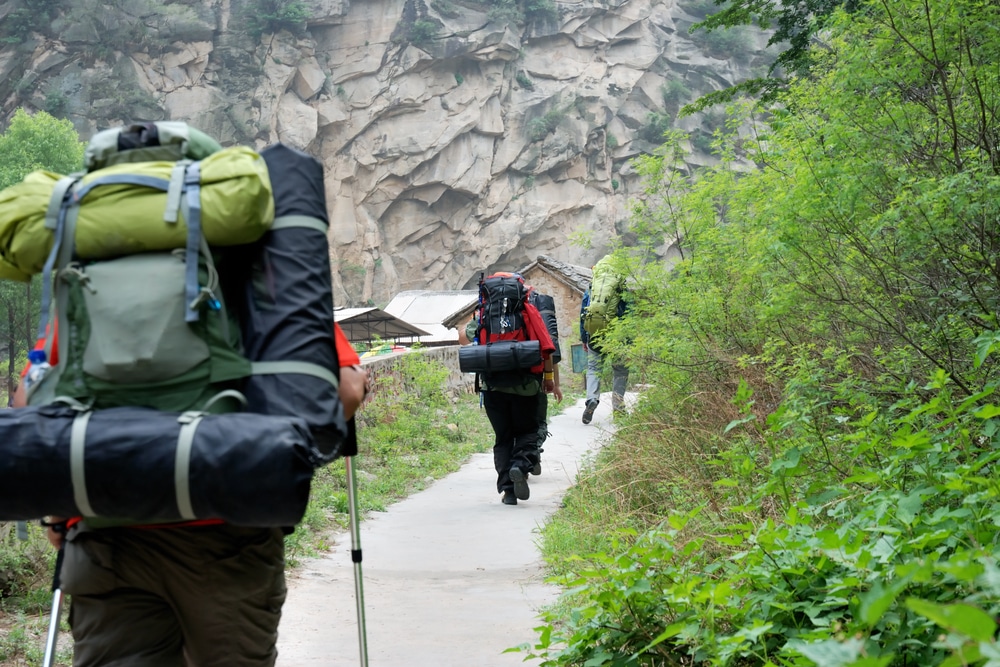 Three individuals hiking towards a mountain carrying large backpacks and camping equipment