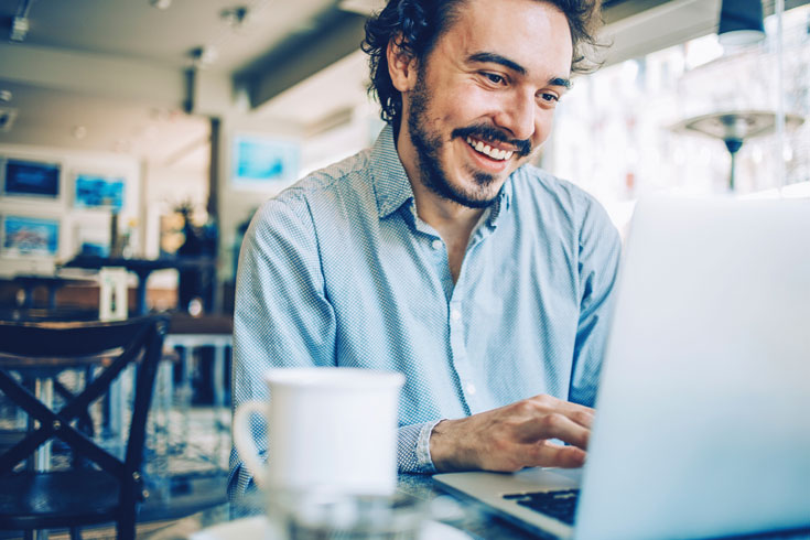 man in a cafe on a laptop smiling while he's working