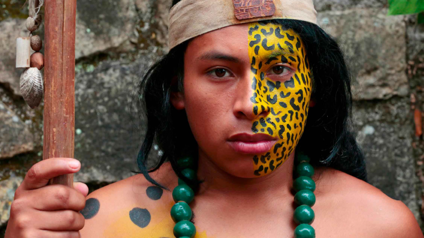 portrait of an indigenous Indian holding a staff with half of his face pained in leopard print